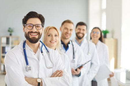 Portrait of happy successful team of young doctors in white uniform looking cheerful at camera and smiling while standing in hospital or clinic. Medical staff and health care concept.の写真素材