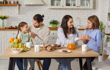 Portrait of happy family of father, mother and kids gathering in kitchen at home together having a breakfast. Young smiling parents with two little children enjoying family dinner.の写真素材