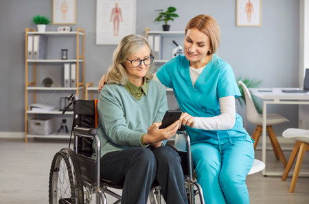 Woman nurse teaching female senior handicapped female how to download health app on smartphone,...