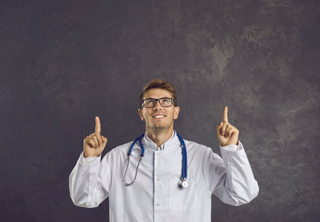 Smiling young male scientist or doctor in white coat show point at empty blank copy space, isolated on black studio background. Happy man GP recommend good promotion offer or sale deal in medicine.の写真素材