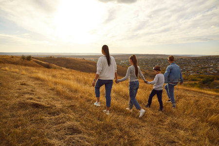 Back view of family holding hands and walking on field during sunset, spending free time outdoors, strolling in nature, enjoying quiet autumn day. Family leisure and lifestyle conceptの写真素材