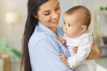Closeup portrait of smiling happy young mother holding little cute baby in hands standing at home. Joyful woman with child indoors. Mothers day, maternity, love and family care concept.の写真素材