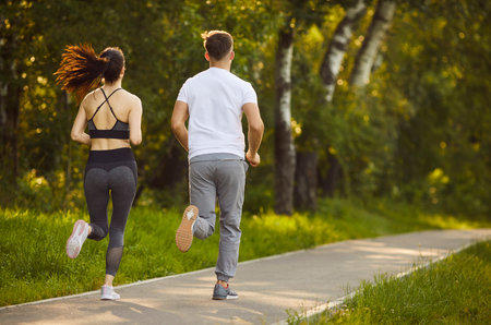 Sport workout and outdoor run of active couple, two fit people jogging in summer green park in morning. Back view of sporty woman and man running together along path. Sport training, wellbeing conceptの写真素材