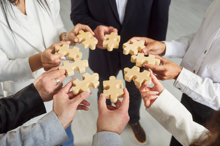 Close-up group of businesspeople engaged in teamwork and problem-solving, holding wooden puzzle pieces, symbol of collaboration, unity in business. Concept of contribution to achieve common goalの写真素材