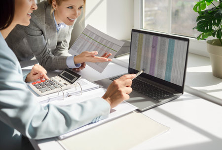 Concentrated businesswomen, female traders looking at laptop screen with stock market data, using computer display graph and chart, analyzing investment to check trading stock information, planningの写真素材