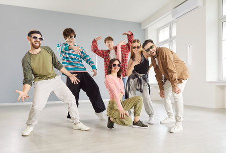 Team of talented young people posing in dance studio, wearing casual clothing and trendy sunglasses,...
