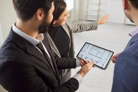 Architect or interior designer showing on tablet new apartment online plan to couple at meeting, realtor consulting customers making real estate offer, mortgage loan investment, repair planningの写真素材