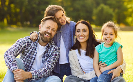 Happy family together in green summer park, outdoors posing for portrait, embracing, showing...