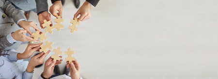 Group of business people standing in circle and holding wooden jigsaw puzzle. Top view of hands of company employees stacking pieces during teamwork activity. Unity and collaboration concept. Banner.の写真素材