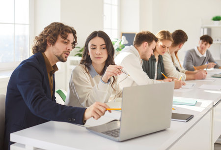 Portrait of young college or university students group sitting in the classroom looking at the laptop monitor screen working on educational project together. Education and knowledge concept.の写真素材