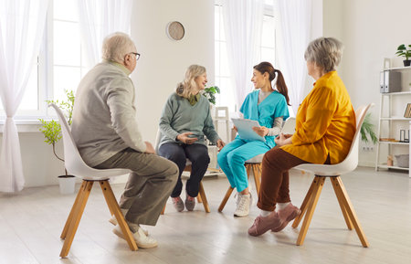 Group of senior people from retirement house sitting in circle and listening advice of nurse, listening attentively speaker, talk about rehabilitation and health. Psychological therapy sessionの写真素材