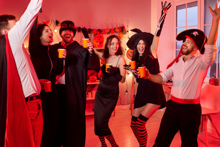 Group of cheerful friends celebrating halloween during night party, dancing to music together in a lively setting, focusing on leisure and fun in a festive atmosphere with engagement.の写真素材