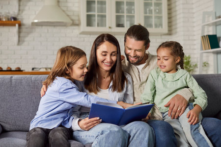 Cheerful family reading a book. Happy parents and children enjoying an interesting story. Smiling mother, father and kids sitting on the sofa in their house or apartment and reading togetherの写真素材