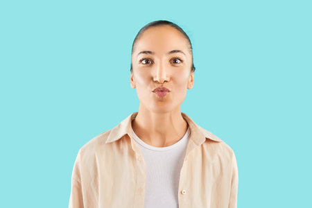 Portrait of a young pretty woman wearing casual clothes posing with kiss face expression standing isolated on studio blue background with copy space and looking at camera. People and emotions conceptの写真素材