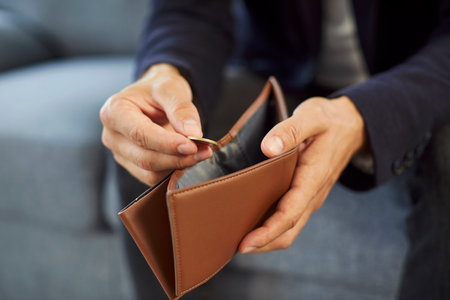 Close up of poor unrecognizable unemployed business man sitting on sofa at home wearing suit and putting coin into empty wallet. Bankrupt, no money, financial crisis and cost control conceptの写真素材