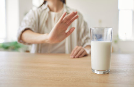 Cropped view of woman sitting at table and making stop gesture with hand toward glass of cow milk. Female person having allergy, discomfort or intolerance to lactose refusing from dairy product.の写真素材