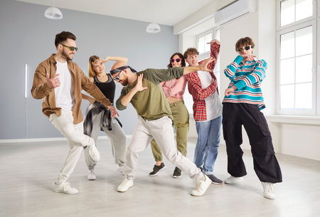 Group of trendy young people dancing together in modern dance studio. Stylish dancers performing hip hop moves, expressing energy and creativity while having fun during dance practice session.の写真素材