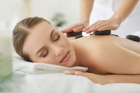 Therapist conducts stone massage session for woman patient in spa salon, focusing on luxury treatment for relaxation during care in a professional setting with emphasis on wellness.の写真素材