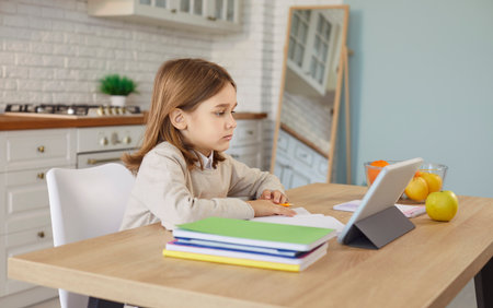 Child doing homework with tablet and paper notebooks, learning online on school lesson, sitting at...