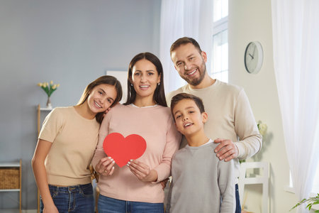 Portrait of a happy and smiling family with two kids holding a red heart, symbolizing love and affection at home. Bonding, softness, and the warmth of family relationships in a joyful moment.の写真素材
