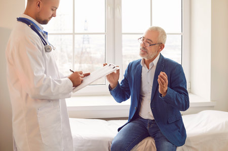 Senior male patient is having a consultation with a doctor or nurse during a visit to the hospital...