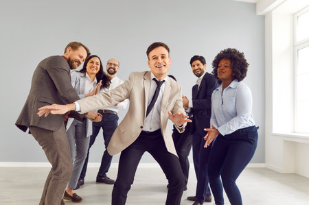 Happy businessman dancing surrounded by a team of colleagues in the office during meeting,...