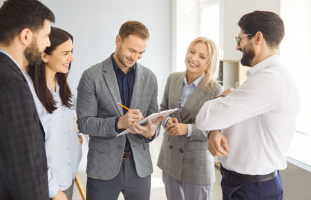 Group of cheerful people company employees discussing work project standing in office during a...