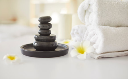 Spa set, rolled towels, stack of hot stones on tray, asian flower tranquil arrangement, relaxation and wellness, therapeutic calm, atmosphere of peaceful spa experience awaiting client in clinicの写真素材