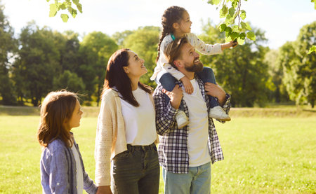 Portrait of happy smiling family with son and daughter standing in summer park walking together...