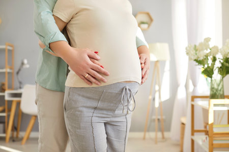 Loving couple belly hug, future parents expecting first baby close standing at home, caring husband...