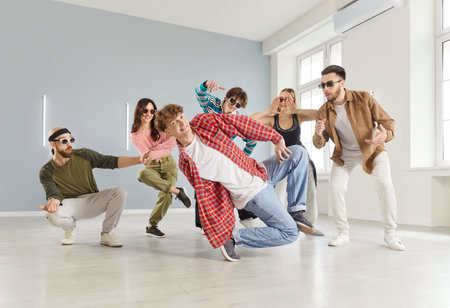 Lively group of young adults girl and guys dressed in casual streetwear, dancing energetically in a...