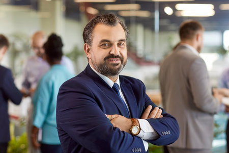 Portrait of confident bearded mature businessman in suit, standing with crossed arms, after...