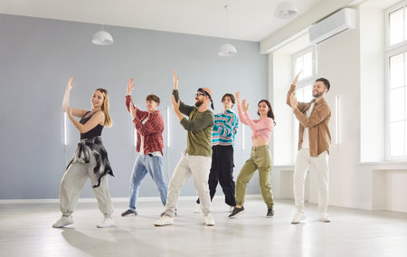 Modern indoor dance studio class, diverse group of dancing young people actively following trainer...