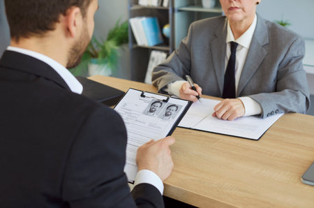 Man job seeker sitting back at the desk holding cv resume and talking to female mature elderly HR manager in office at meeting. Recruitment, human resources and employee recruit concept.の写真素材