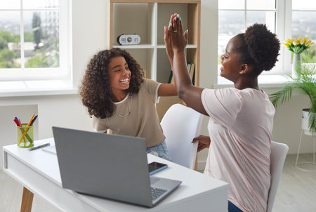 Family teamwork. Happy mother and daughter having fun during homeschooling and giving high-five to...