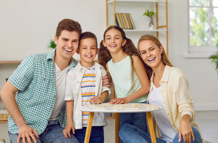 Happy family with two children playing puzzles at table sitting on floor at home in weekend looking...