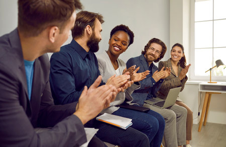 Colleagues applauding for man for a good idea on a working meeting sitting on chairs in row in...