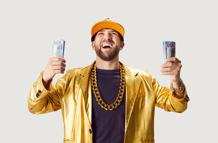 Portrait of happy excited funny young man in golden suit and cap holding money dollars cash...