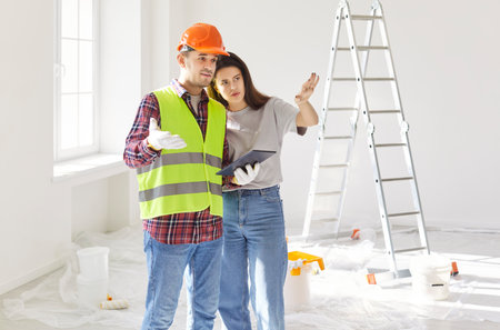 Construction worker in reflective vest and hard hat holding tablet, discussing renovation plans with...