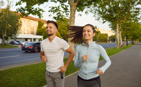 Active fit sporty couple running energetically along an urban sreet sidewalk, jogging in motion near...