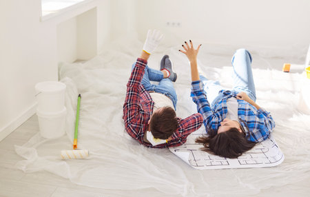 Smiling young family couple lying on floor and discussing design ideas for their new home. Relaxed man and woman enjoying break from renovation work while planning creative improvements together.の写真素材