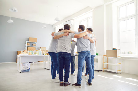 Team of young volunteers standing in circle and hugging. Diverse group standing together, supporting...