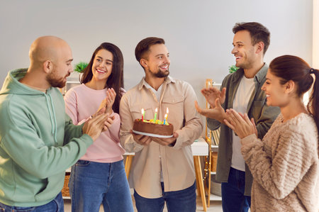Group of friends celebrates a man birthday at home, surprising him with a cake adorned with candles....