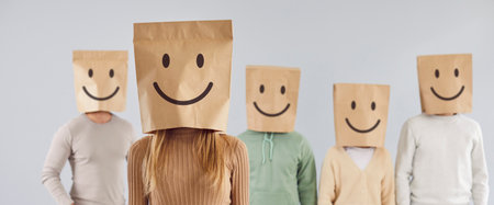 Group of unidentified people carry paper bags with smiley emoticons painted on heads. Portrait of woman with positive emoticon instead of face standing in front of group of people on gray background.の写真素材