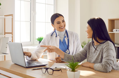 Female young woman patient visiting a smiling friendly doctor at the medical office in hospital, looking at the laptop monitor screen and having consultation during medical examination in clinic.の写真素材