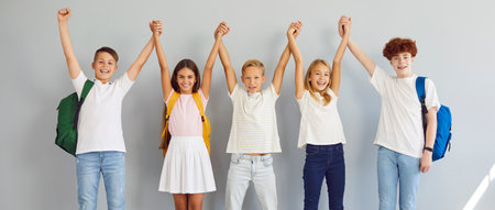 Happy smiling group of school kids in casual clothes standing together in a row holding hands up...
