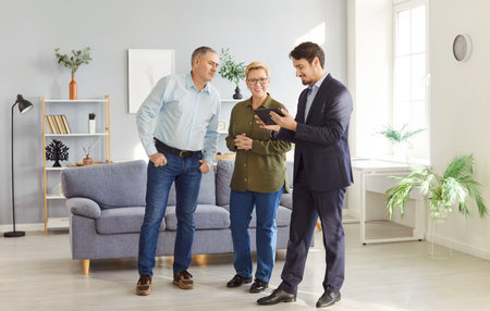 Male real estate agent or realtor guides a senior couple through a new property or apartment, assisting them in the home buying process. Focus is on finding the perfect new accommodation.の写真素材