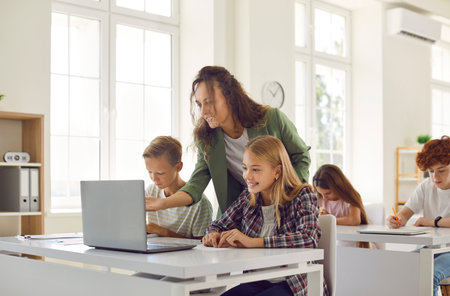 Group of junior high school students and classmates sitting at the desk in the classroom with female friendly smiling teacher showing something on laptop. Education and back to school concept.の写真素材