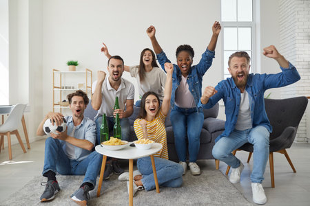 Multinational group of friends of fans gathered in front of the TV to watch a football match...