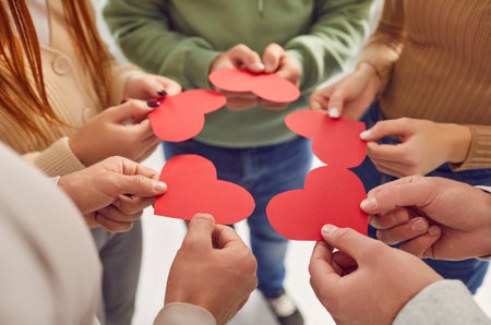 Close up view of a diverse group holding red hearts in hands, forming a circle of love and unity....